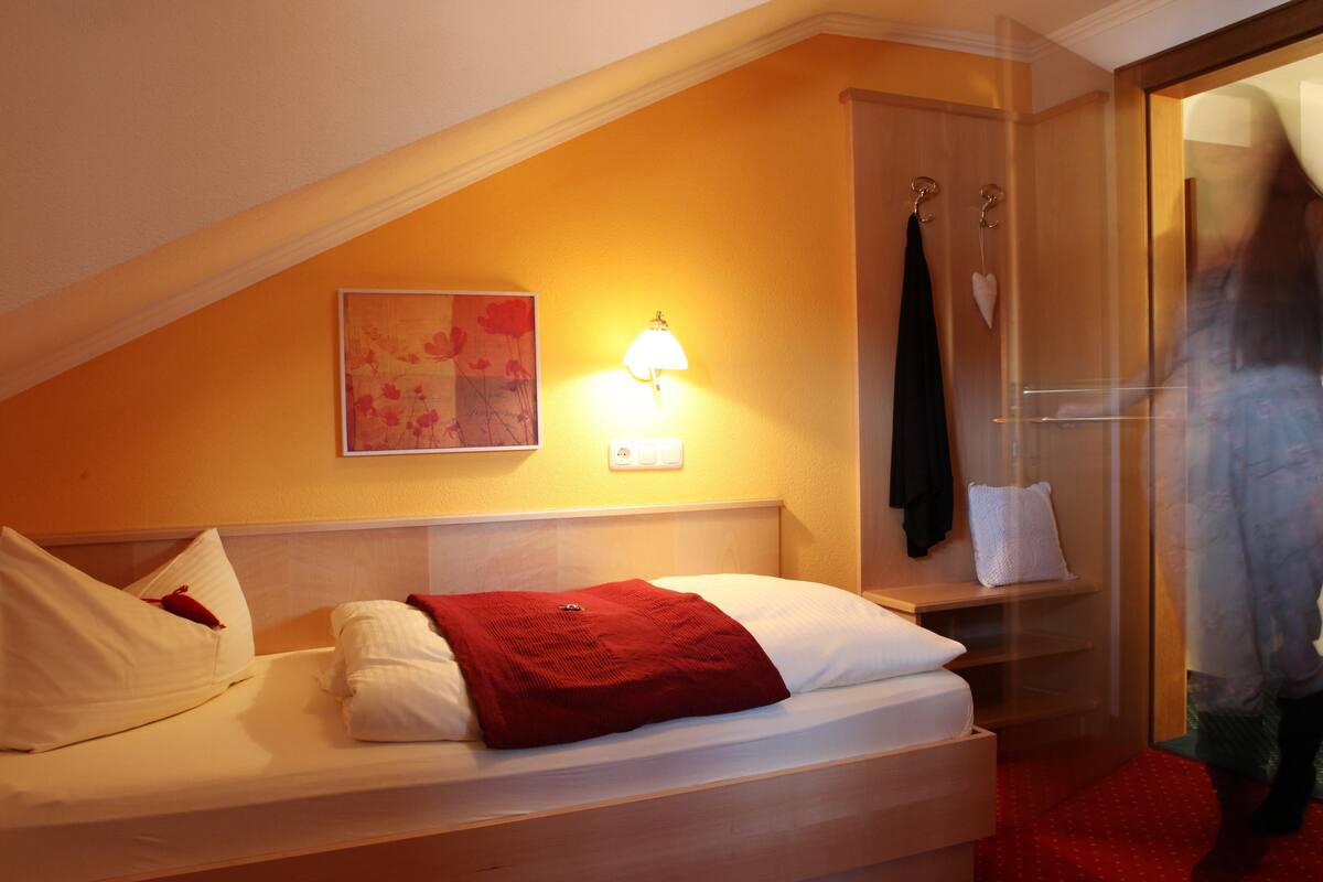 A hotel room with a bed, a wall-mounted lamp, a painting, and a robe hook.
