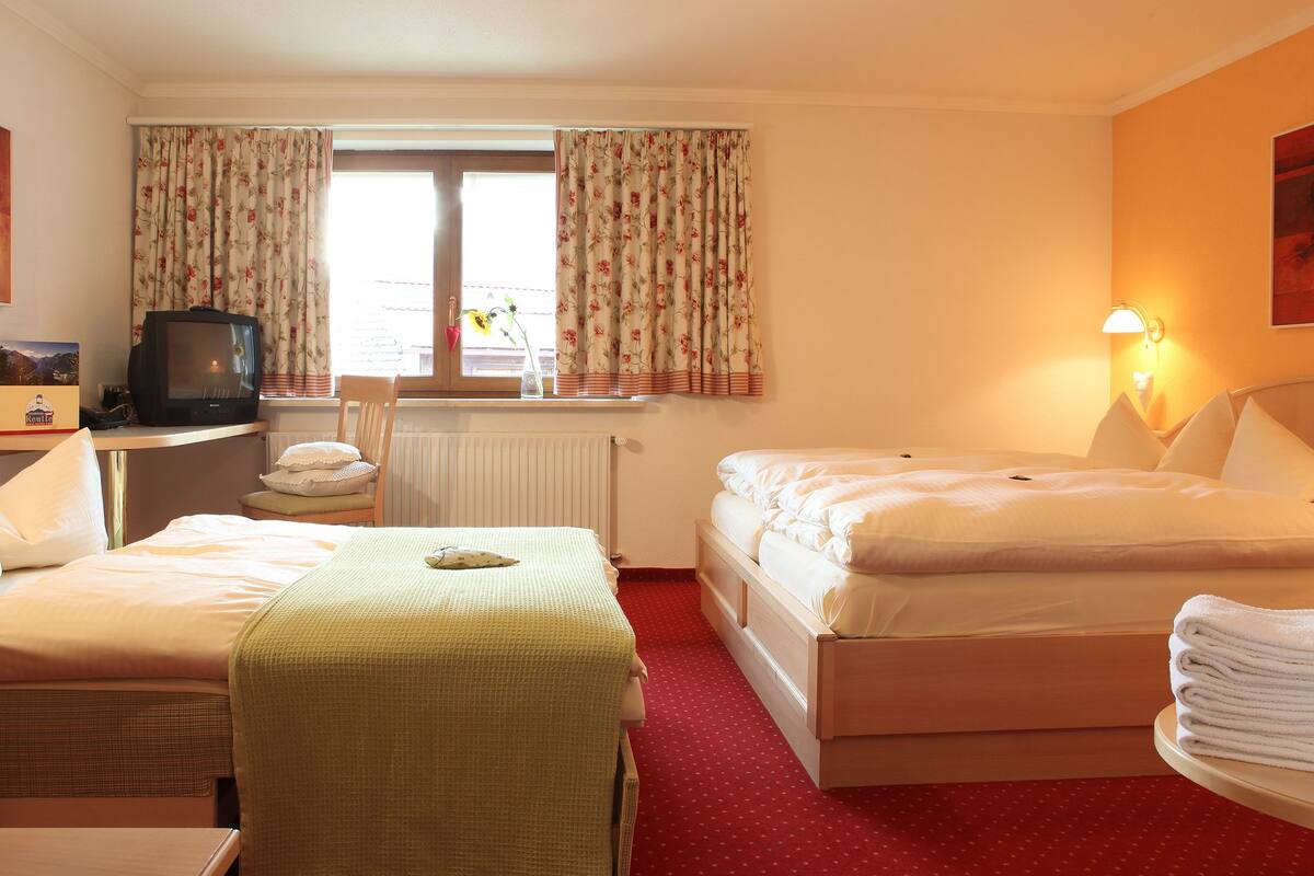 A hotel room with two beds, a desk with a television, a chair, a radiator, and a lamp.
