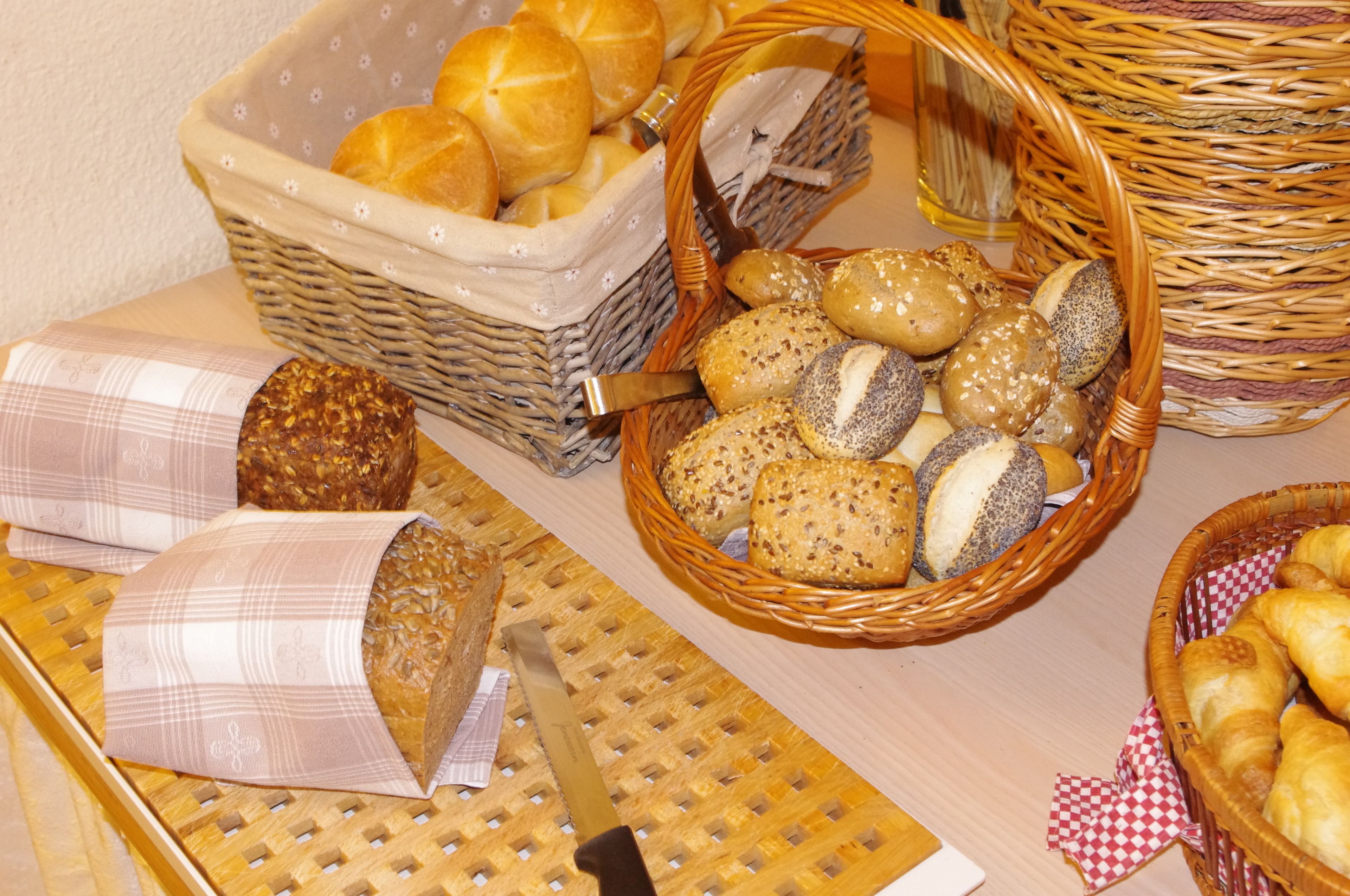 A table with various types of bread and pastries in wicker baskets.