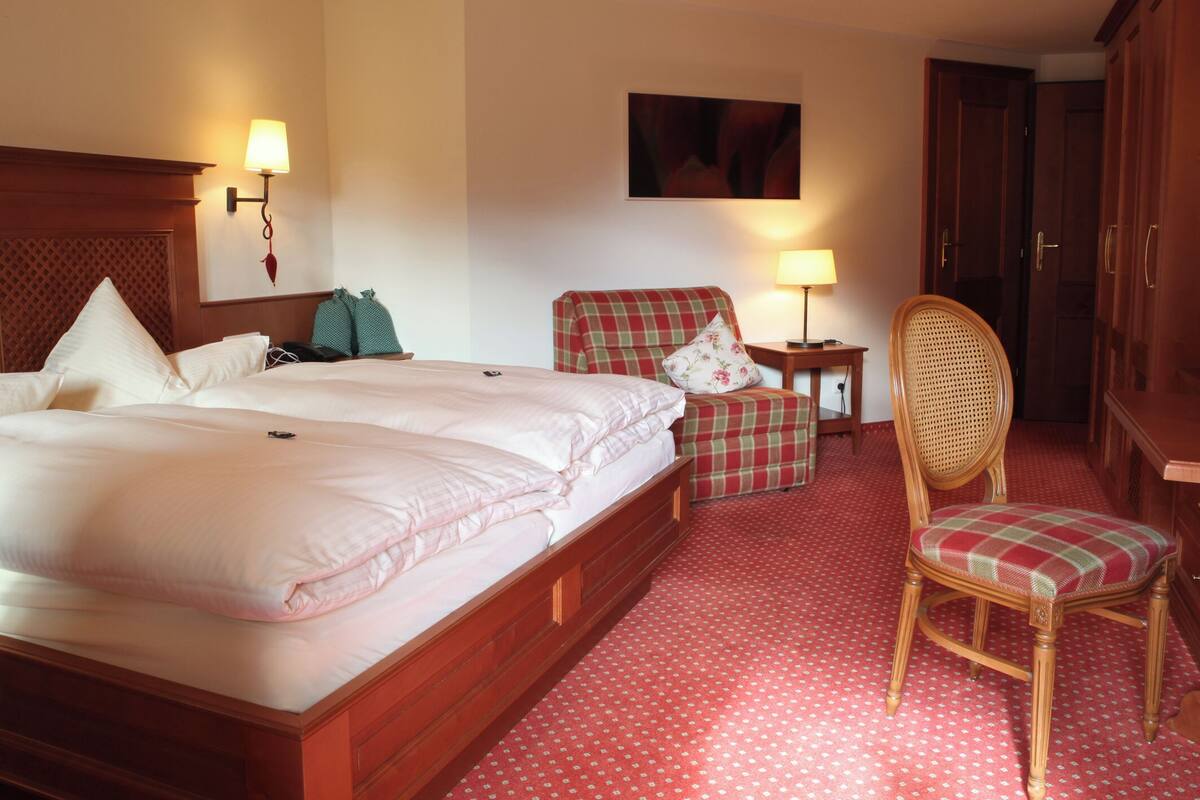 A hotel room with a large bed, a chair, a small table, and a wardrobe.