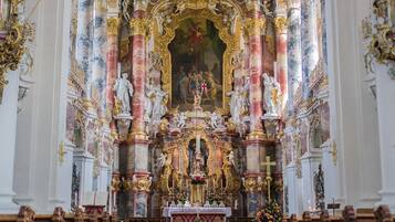 Interior de igreja ornamentado, com altar central, estátuas e arranjos florais.