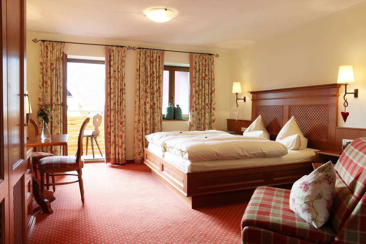 A hotel room with a bed, a chair, a table, and a view of the outside.