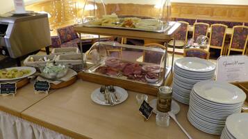 Montaje de bufé con diversos alimentos, incluyendo carnes y quesos, y un letrero que dice 'Guten Morgen!'.
