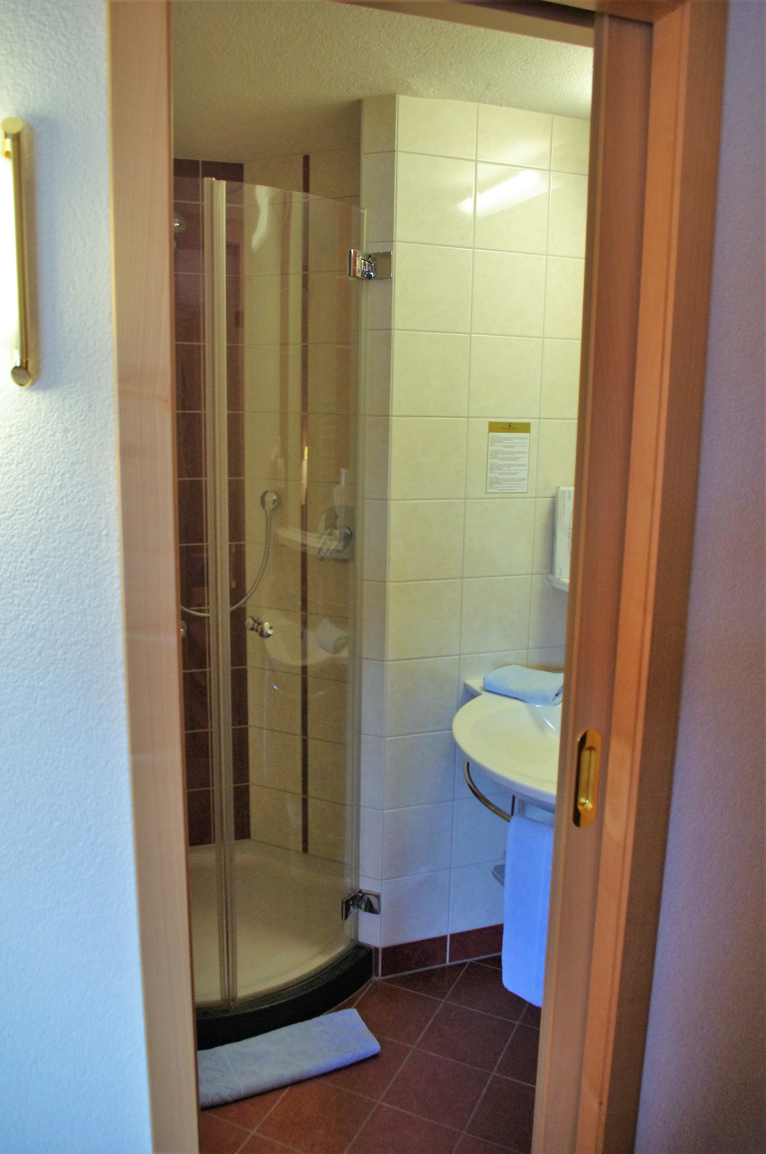 Ein Badezimmer mit einer gläsernen Duschkabine, einem weißen Waschbecken und einem gefliesten Boden.