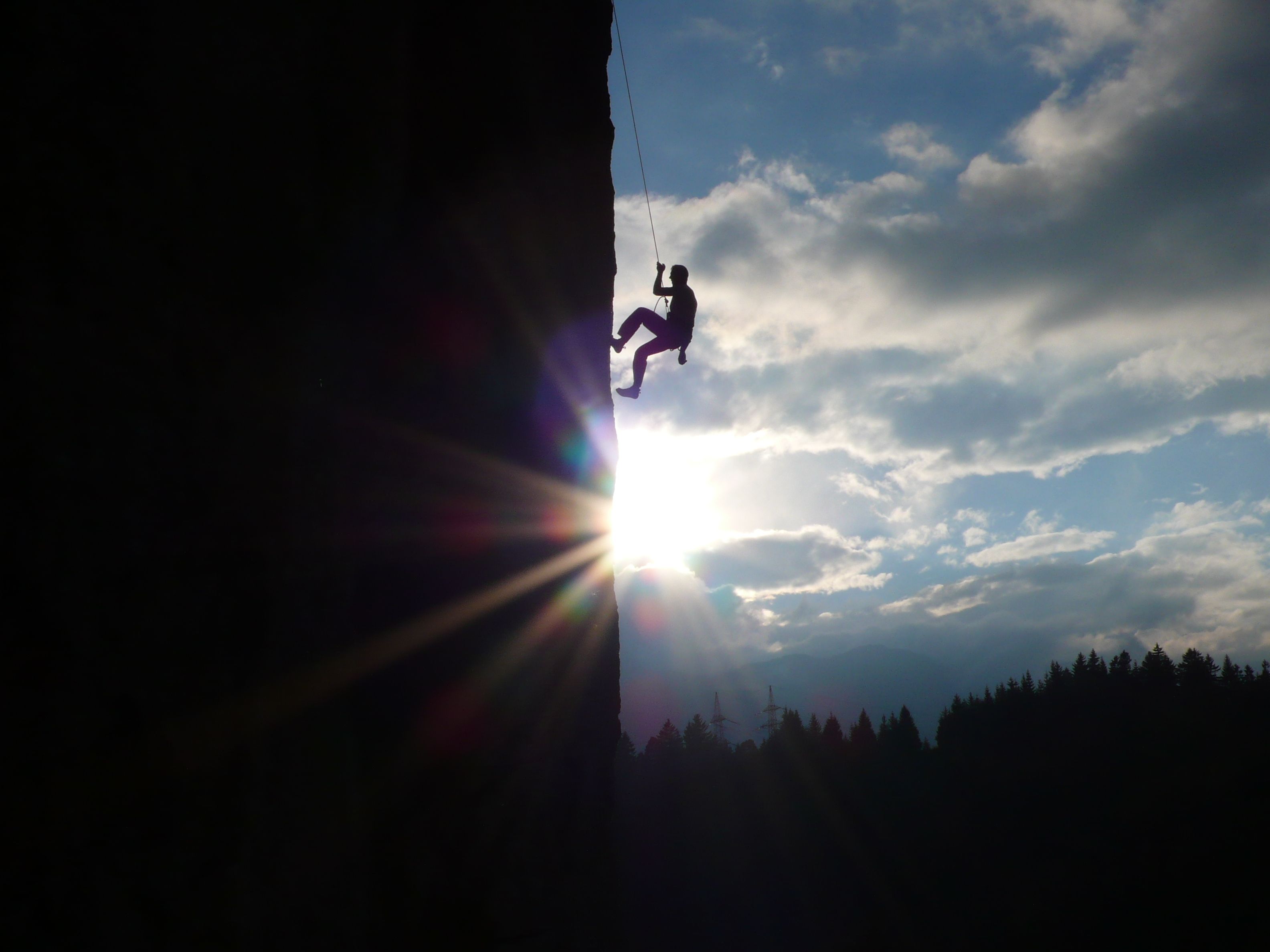 Une personne qui descend une falaise en rappel, avec le soleil qui brille à l'arrière-plan.