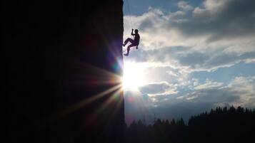 Une personne qui descend une falaise en rappel, avec le soleil qui brille à l'arrière-plan.