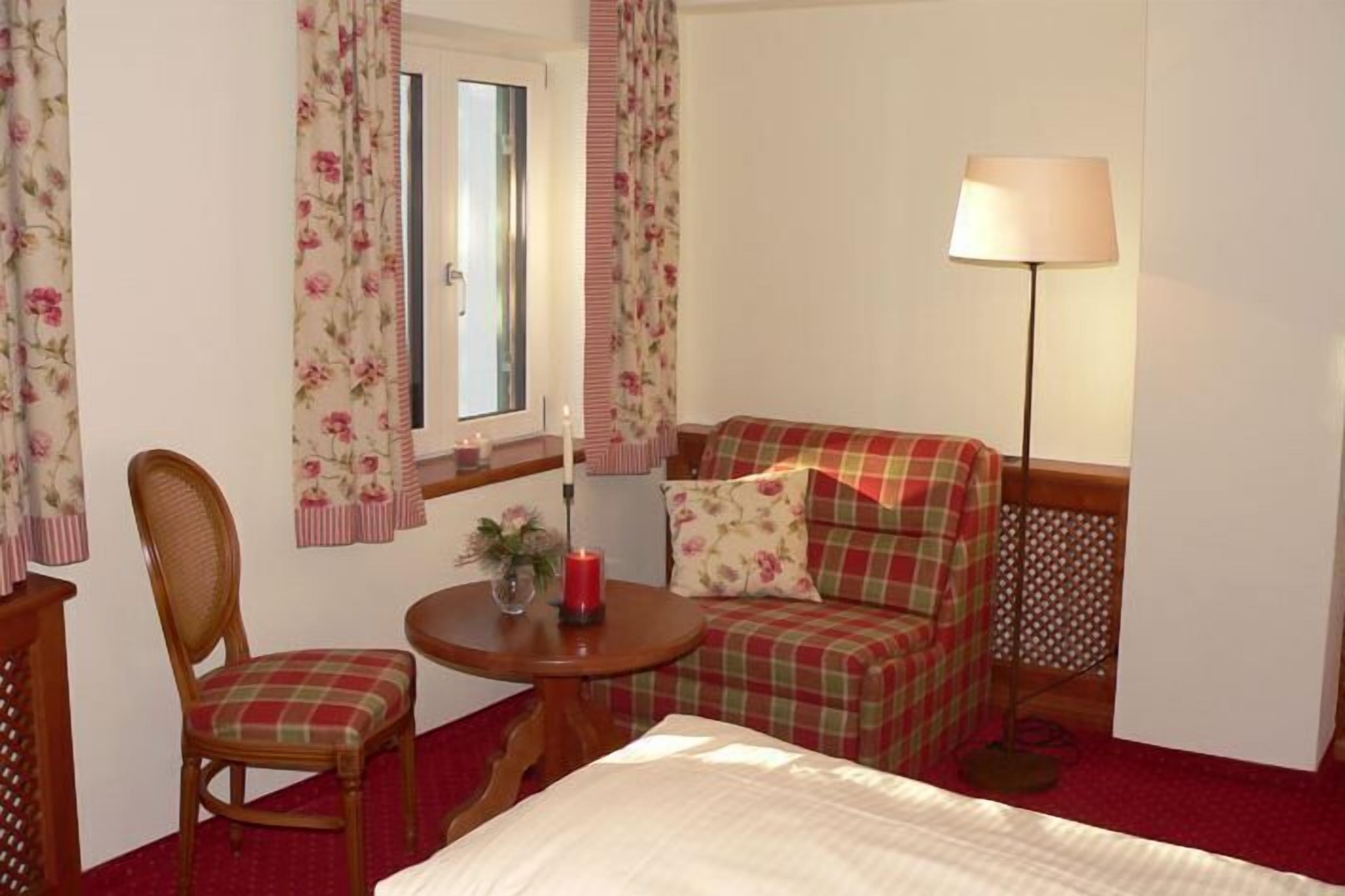 Ein Hotelzimmer mit einem Bett, einem Sessel, einem kleinen Tisch mit Kerze und einer Lampe.