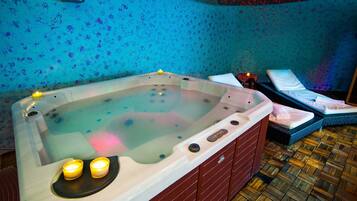 A hot tub with two candles, a massage chair, and a wooden floor.