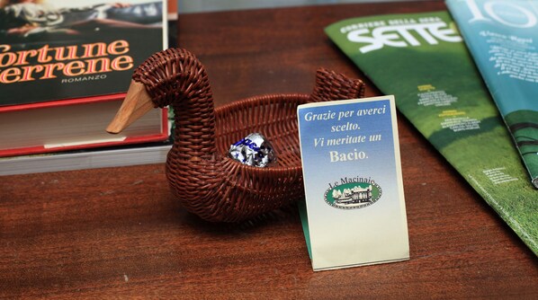 Un recipiente con forma de cisne de mimbre sostiene una estrella de plata, sobre una superficie de madera con libros y un letrero en italiano.