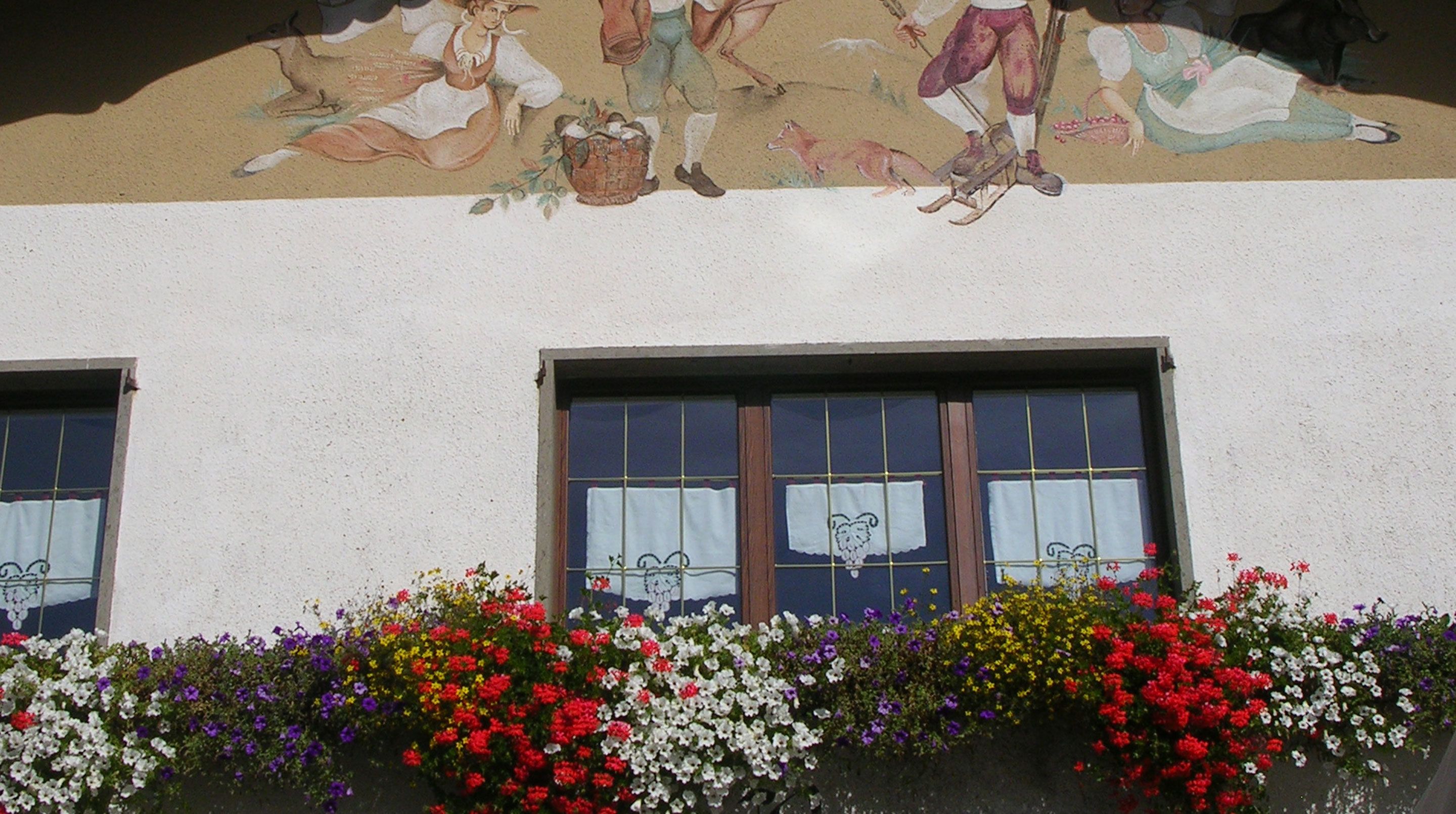 A building facade with a mural depicting rural scenes and a row of windows with white curtains.
