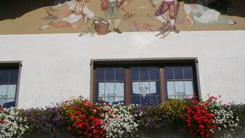 Fachada de edificio con un mural que representa escenas campestres y una hilera de ventanas con cortinas blancas.