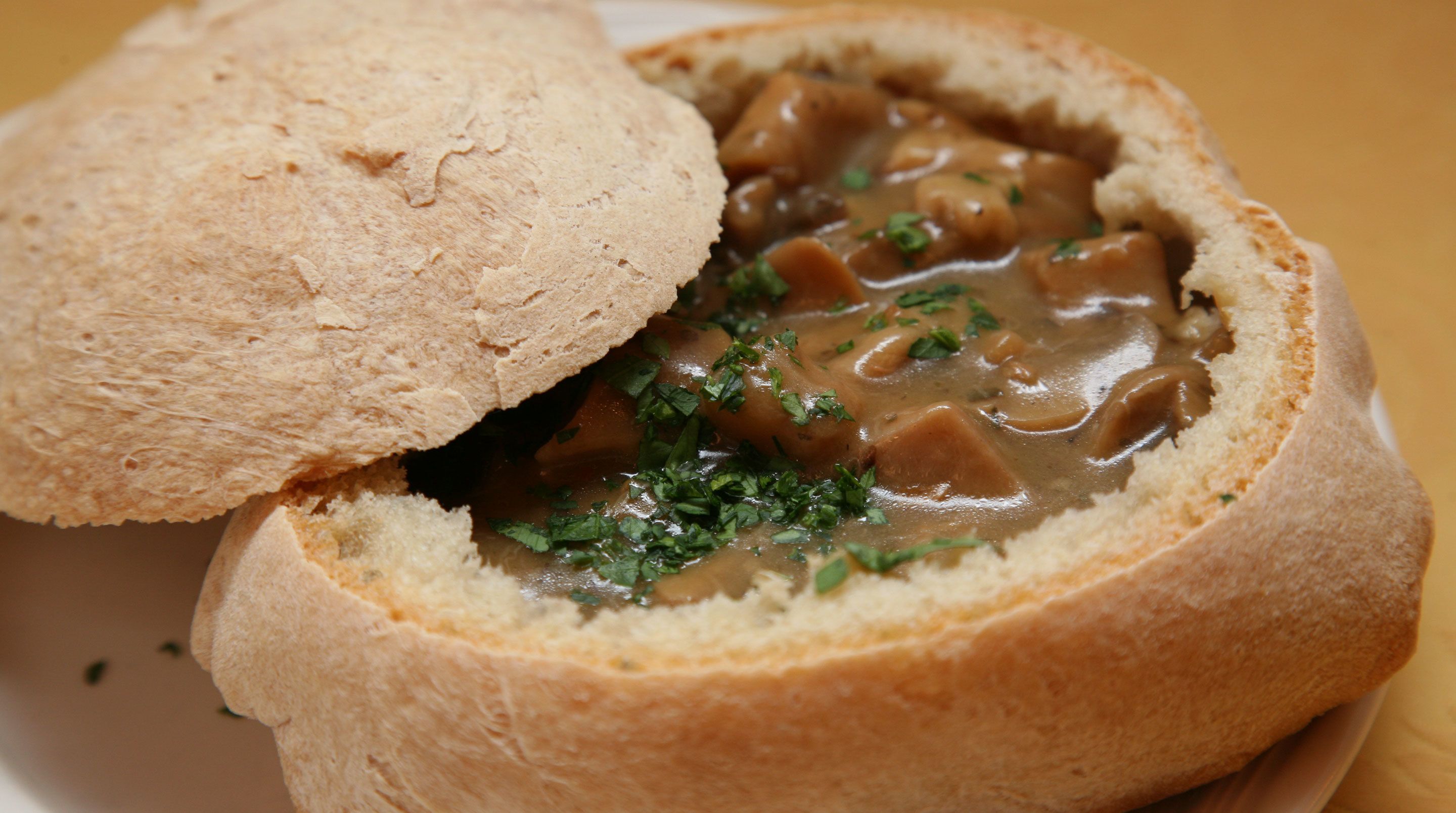 A sandwich with a bun cut in half, filled with a brown sauce and green herbs.