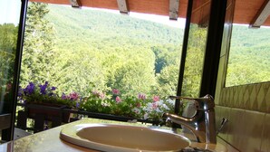 Ein Badezimmer mit einem Waschbecken und Blick auf einen bewaldeten Berg durch ein Fenster.