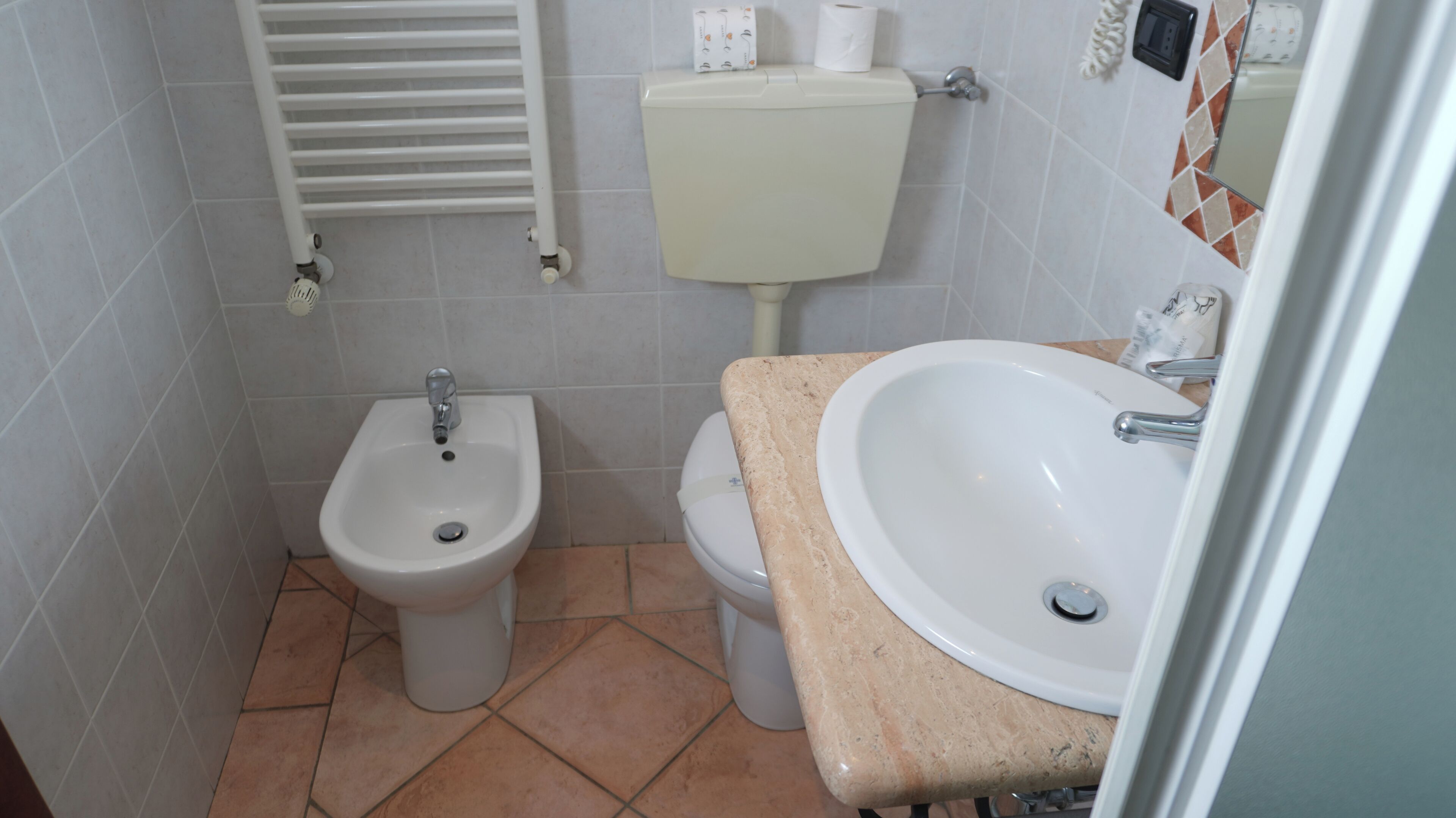Un baño con bidé, inodoro, lavabo y suelo de baldosas.