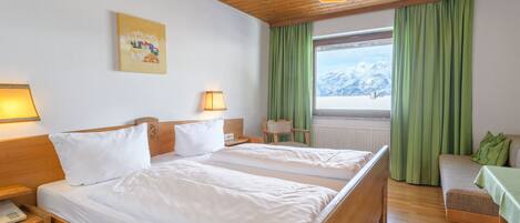 Une chambre d’hôtel avec deux lits, des têtes de lit en bois, un plafond en bois, une fenêtre donnant sur les montagnes et un rideau vert.