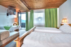 A hotel room with a wooden ceiling, a bed with white linens, a small table with a green tablecloth, a chair, and a television mounted on the wall. - Bärenwirth (Patsch)