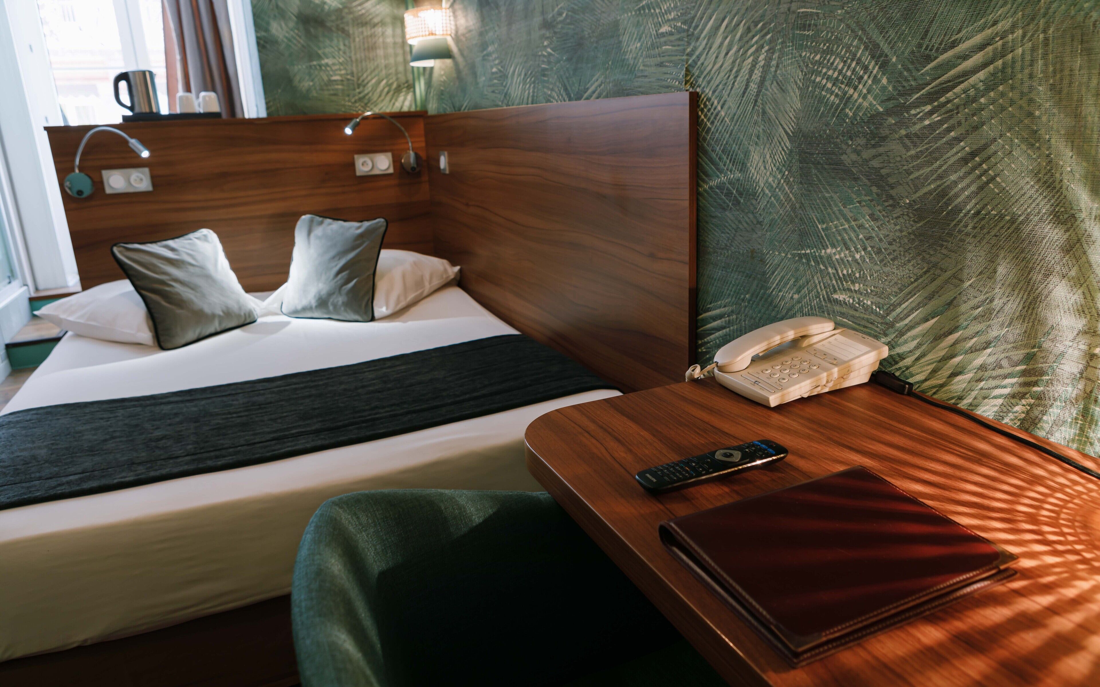 Een hotelkamer met een bed, nachtkastje, lamp en telefoon.