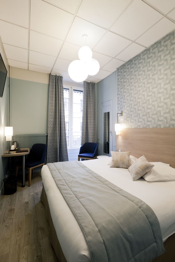 A hotel room with a large bed, two chairs, a desk, a lamp, and a view of the outdoors.