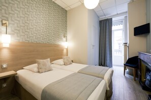 Quarto de hotel com duas camas, cabeceira de madeira, televisão de tela plana, escrivaninha e lareira.