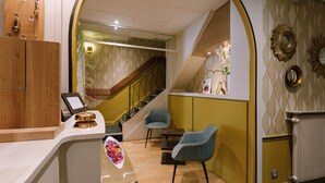 A hotel lobby with a reception desk, two chairs, a staircase, and decorative wall mirrors. - Hôtel du Dauphin (Lyon)