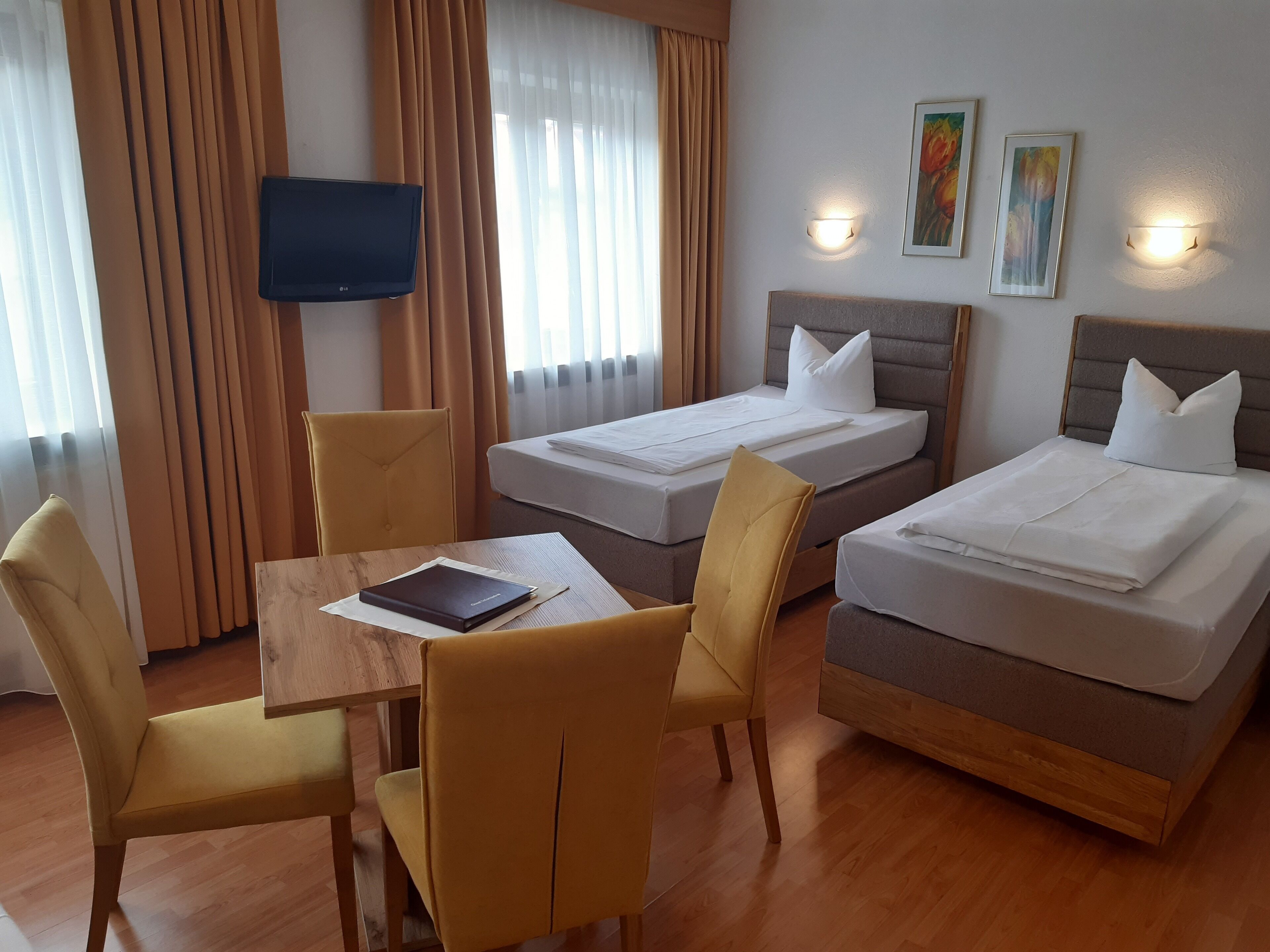 Habitación de hotel con dos camas, un televisor, una mesa con un libro y dos sillas.