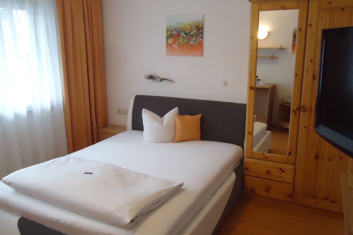 Une chambre d’hôtel avec un lit, une télévision, un tableau au mur et une armoire en bois.
