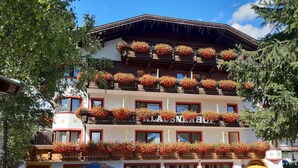 Un hôtel à plusieurs étages, doté de balcons ornés de fleurs rouges, d’une enseigne indiquant « LAUSNERHOT » et d’un jardin bien entretenu.