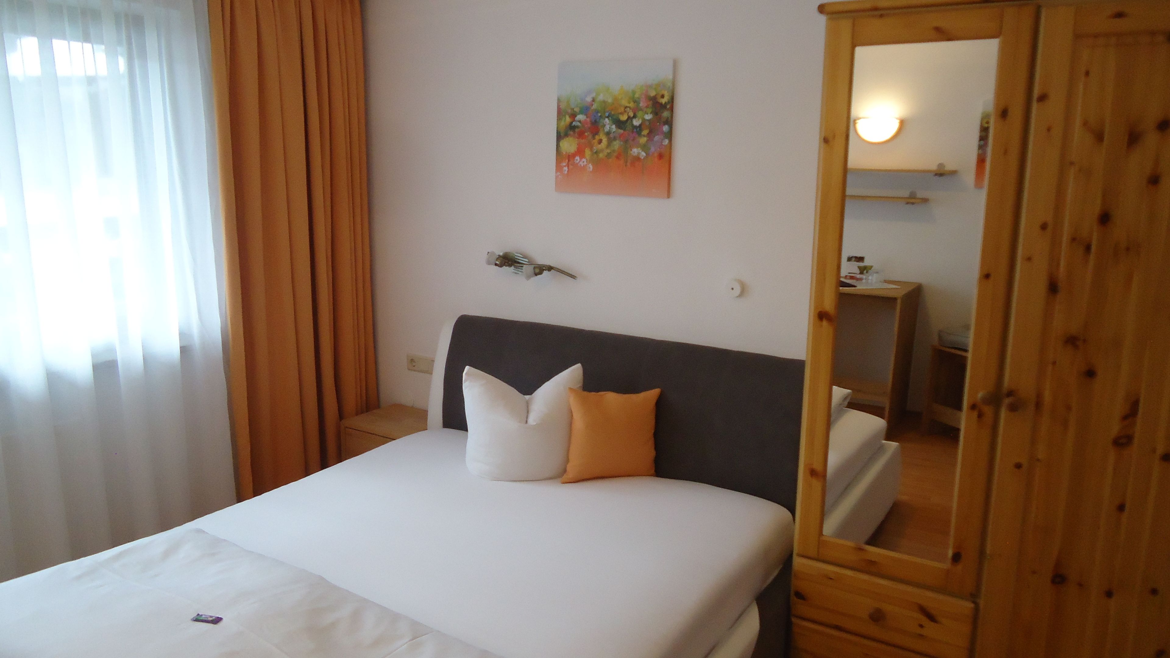 A bedroom with a bed, a nightstand, a mirror, and a painting on the wall.