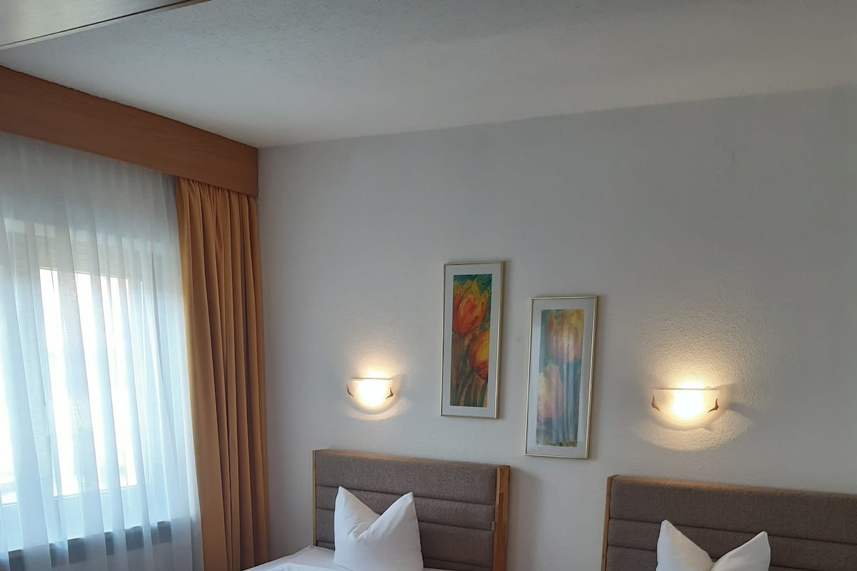 Une chambre d’hôtel avec deux lits, des têtes de lit en bois, du linge de lit blanc et deux appliques murales.