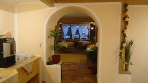 Un couloir mène à une salle à manger où se trouvent une plante en pot, une table en bois et un téléviseur posé sur un meuble.