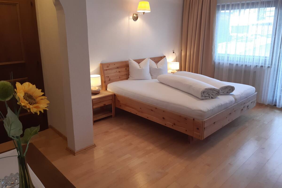 Un lit bien fait, avec une tête de lit en bois, une table de chevet avec une lampe et un vase rempli de tournesols.