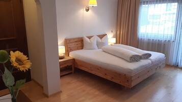 A neatly made bed with a wooden headboard, a nightstand with a lamp, and a vase with sunflowers.