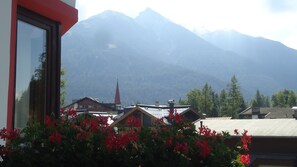 Une vue sur une montagne, avec le clocher d’une église, des maisons et des fleurs rouges au premier plan.
