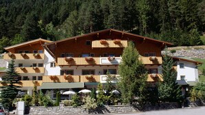 A multi-story hotel with wooden balconies, outdoor seating, and a mountainous backdrop.
