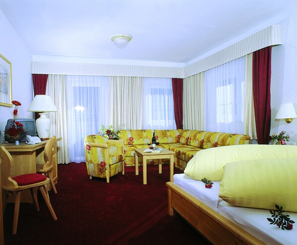 A hotel room with a sofa, a sofa, a chair, a desk, a bed, and a window with curtains.
