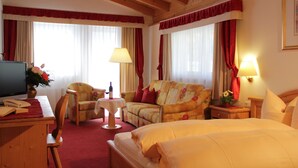 A hotel room with a bed, a sofa, a desk with a lamp, and a TV.
