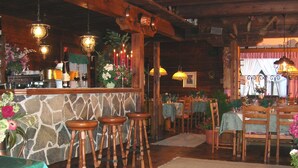 A rustic interior with a stone wall bar area, wooden stools, and tables set for dining.