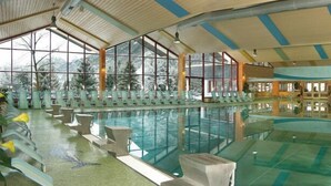 A large indoor swimming pool with clear glass walls, seating areas, and a high ceiling.