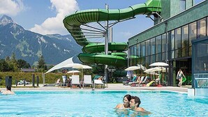 A swimming pool with a green water slide and lounge chairs. - Hotel Tannenhof (Waengle)