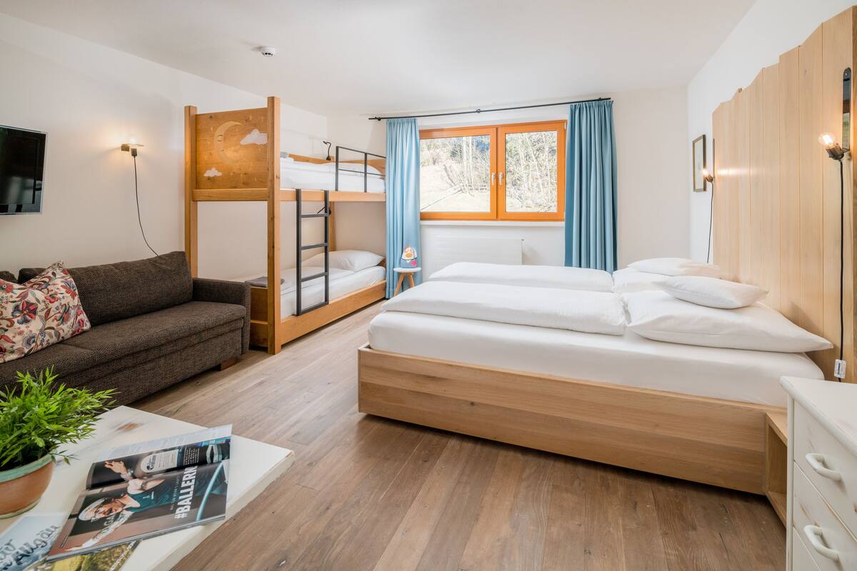Un dormitorio moderno con literas, un sofá, una mesita de noche y una ventana con cortinas.