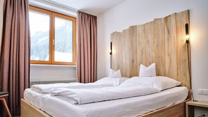 A wooden bed with white bedding, a window with curtains, and a nightstand with a lamp. - Hotel Tannenhof (Waengle)