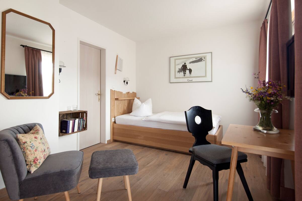 Una habitación pequeña y ordenada con cama, escritorio, silla, estantería y espejo.