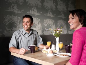 A dining table with breakfast items, a vase with flowers, and a patterned wallpaper background.