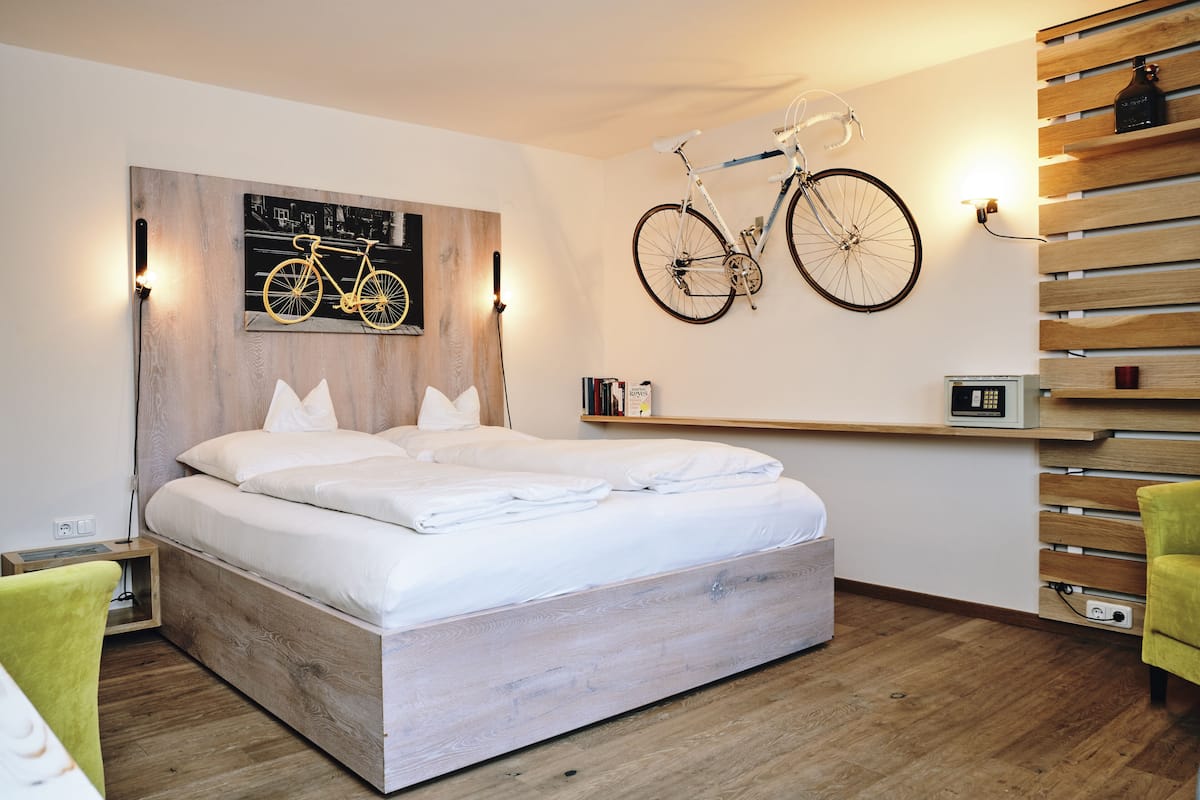 Un dormitorio moderno con una cama de madera, una bicicleta montada en la pared, una estantería con libros y una mesita de noche con lámpara.