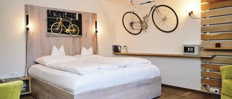 A modern bedroom with a wooden bed, a mounted bicycle, a shelf with books, and a bedside table with a lamp.