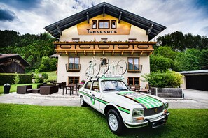 Un hotel con fachada de madera, balcones y un coche blanco estacionado al frente.