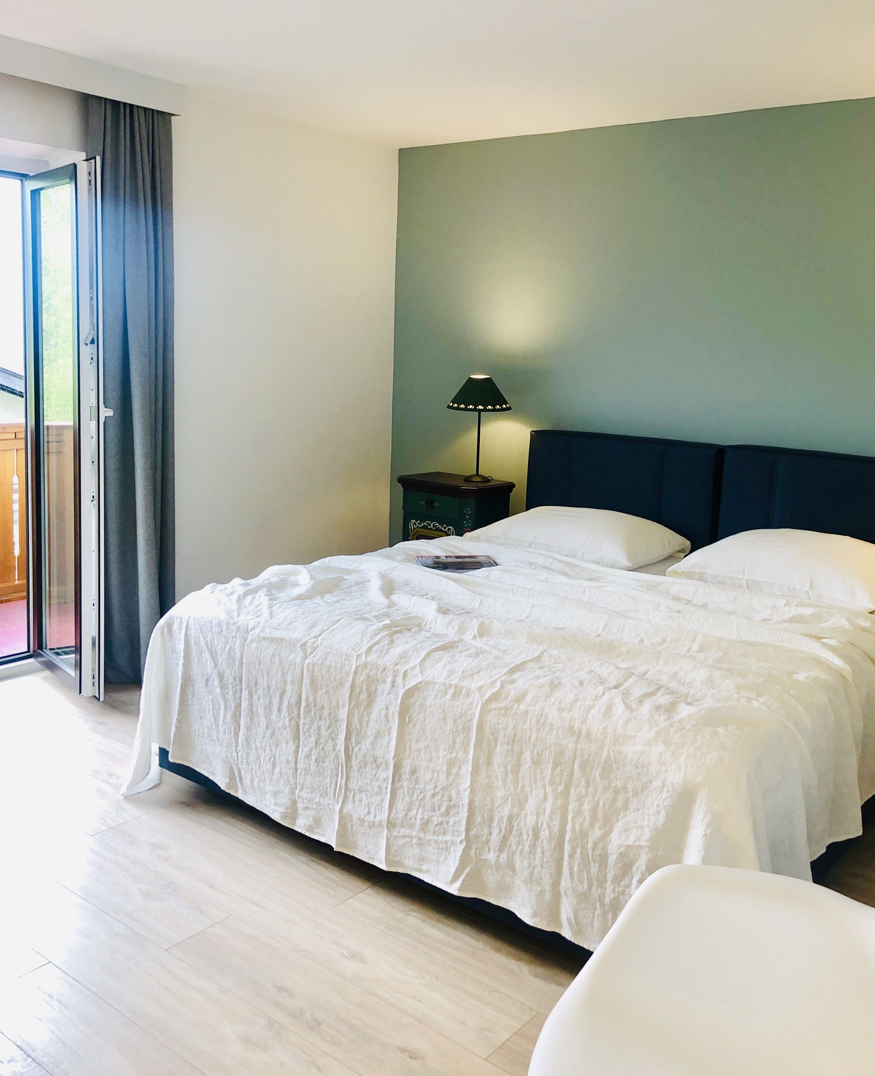 A neatly made bed with white linens, a bedside table with a lamp, and a view of a balcony through a sliding door.