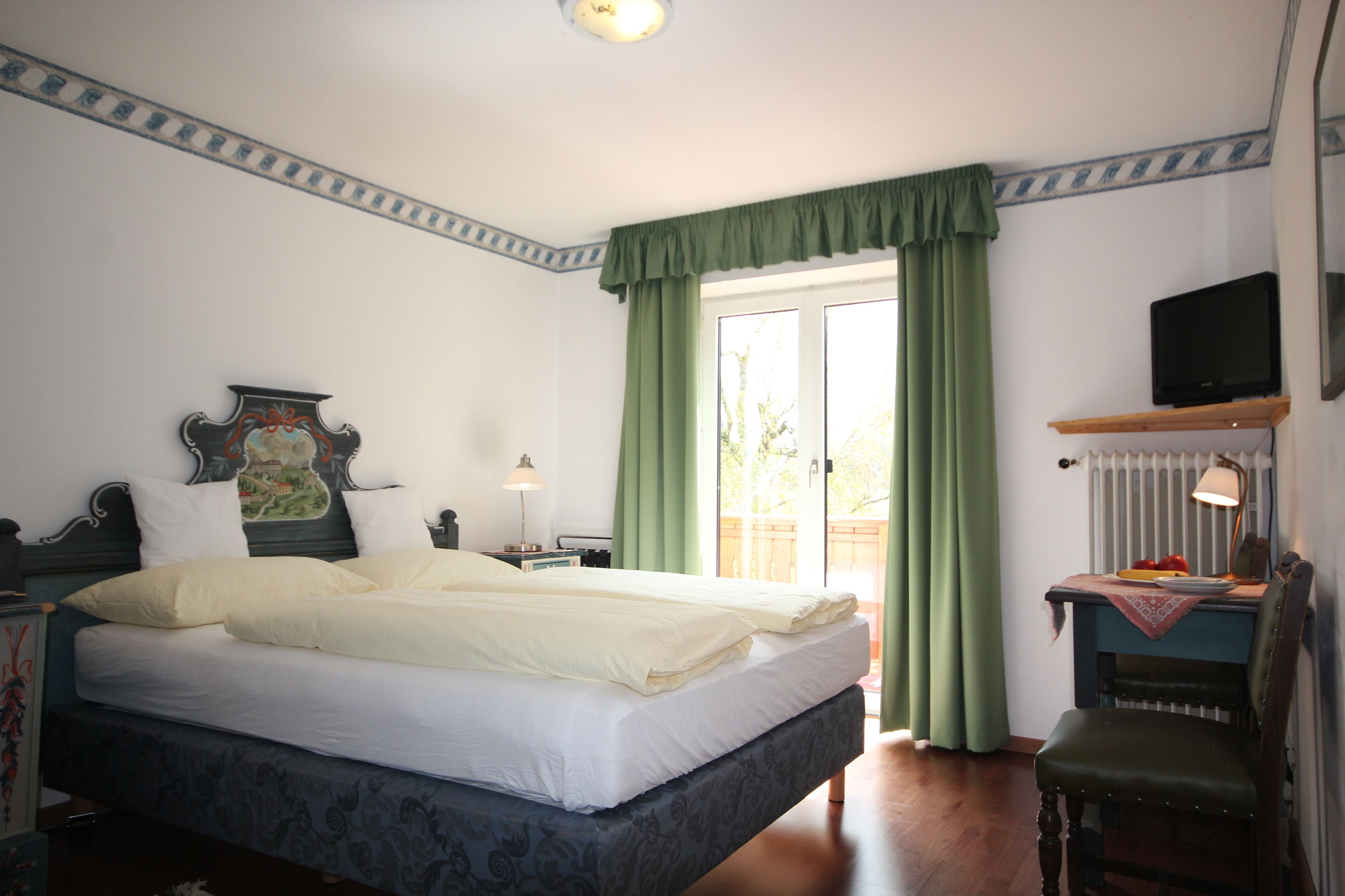 Ein Schlafzimmer mit einem großen Bett, einem Schreibtisch mit Lampe, einem Sessel und einem Fernseher auf einem Regal.