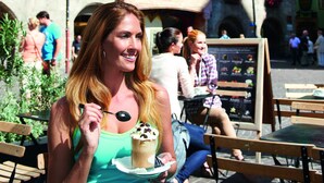 A woman sitting at an outdoor café with a dessert in front of her, in front of a building with flower boxes and a balcony. - Hotel Sonnenhof - bed & breakfast & appartements (Innsbruck)