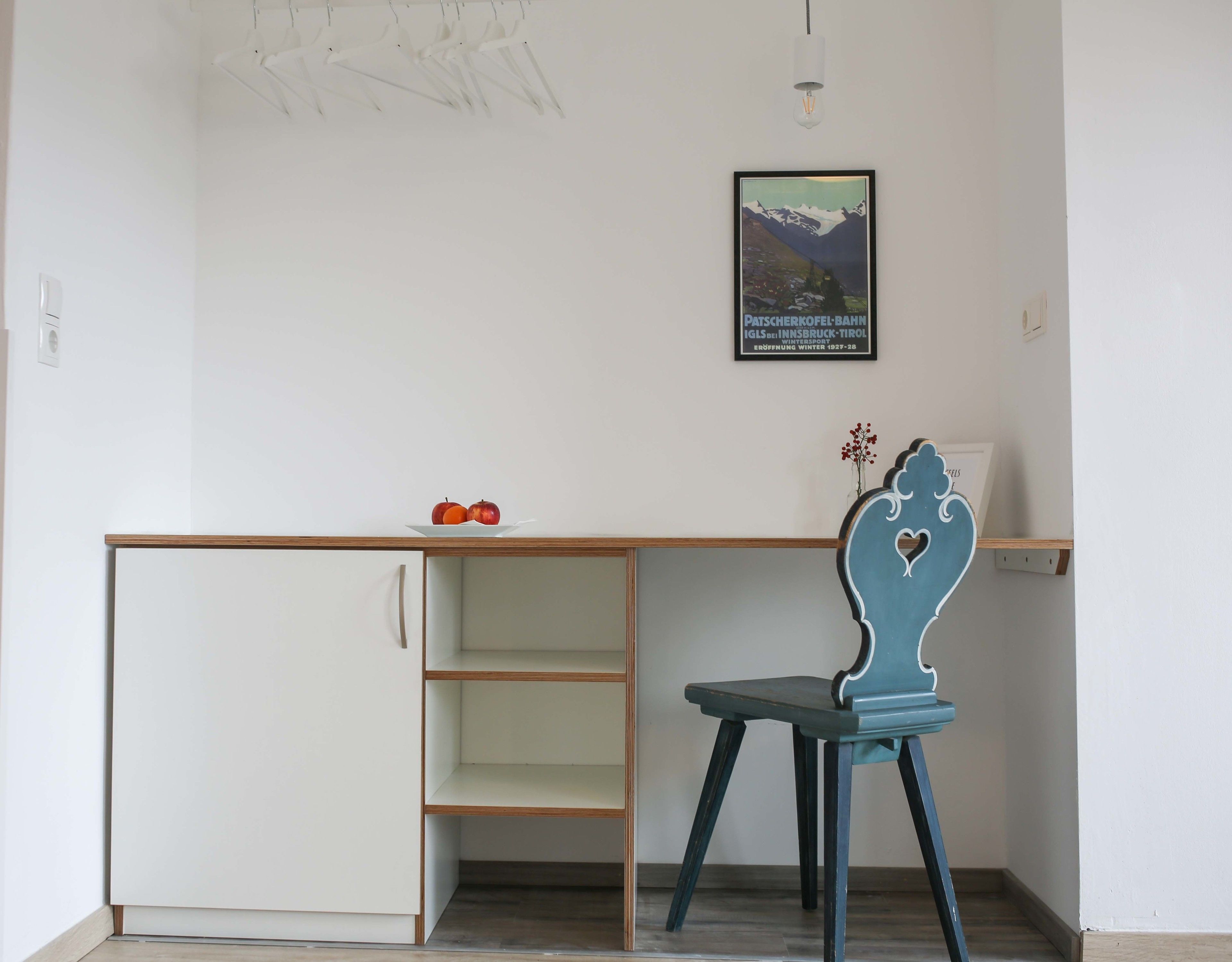 A room with a white cabinet, a blue chair with a heart design, and a framed picture on the wall.